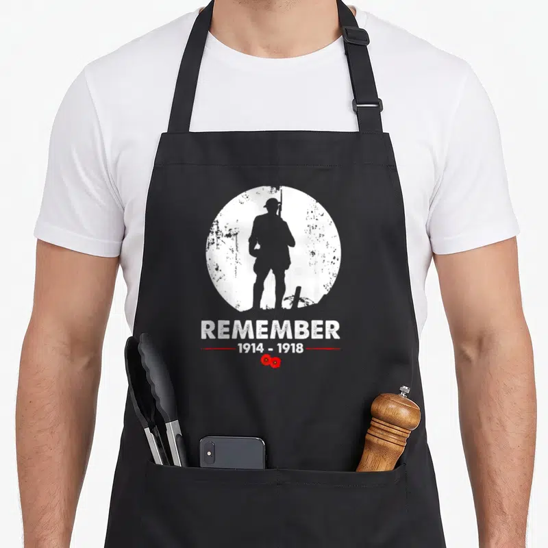 Tablier de cuisine noir avec silhouette soldat, texte Remember 1914-1918 et deux coquelicots rouges en bas du motif circulaire blanc.