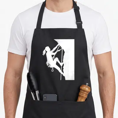 Tablier de cuisine noir avec une femme grimpeuse en silhouette blanche accrochée à une paroi rocheuse stylisée.