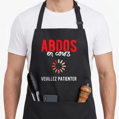 Tablier de cuisine noir avec inscription Abdos en cours et symbole de chargement rotatif rouge et blanc.