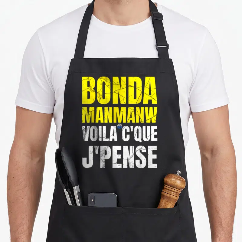Tablier de cuisine noir avec inscription Bonda Manmanw Voilà c'que j'pense en lettres jaunes et blanches texturées.