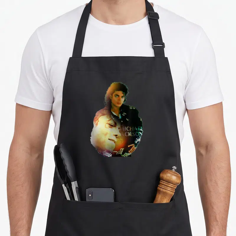 Tablier de cuisine noir avec double portrait coloré de Michael Jackson et son nom imprimé en lettres stylisées sur le torse.
