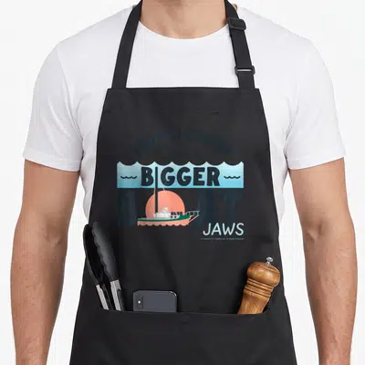 Tablier de cuisine noir avec illustration d'un petit bateau et texte You're Gonna Need A Bigger Boat Jaws en lettres noires et bleues.