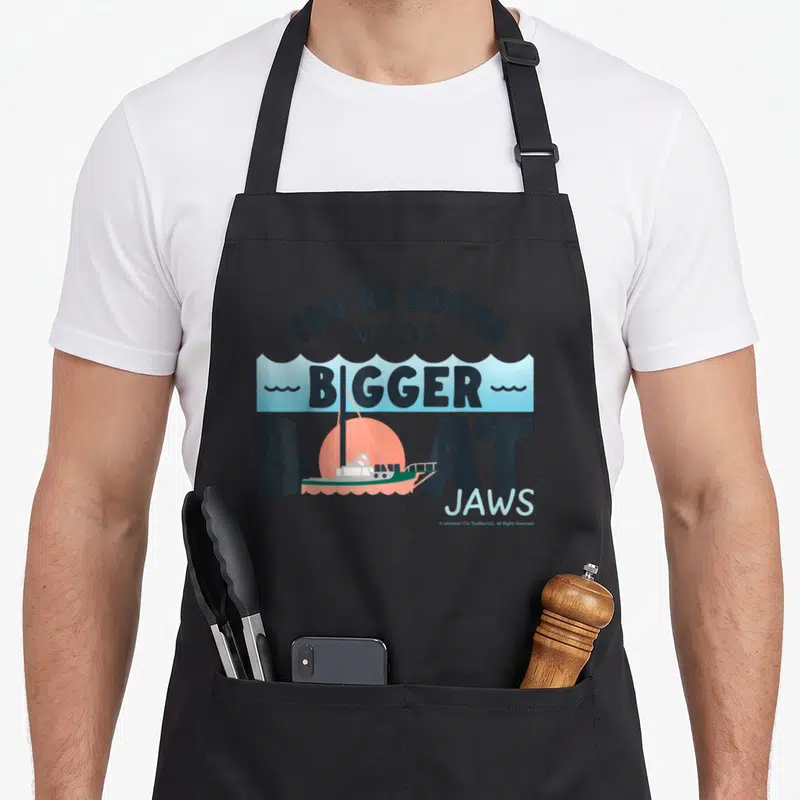 Tablier de cuisine noir avec illustration d'un petit bateau et texte You're Gonna Need A Bigger Boat Jaws en lettres noires et bleues.