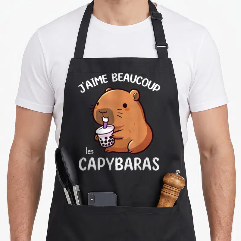 Tablier de cuisine noir avec illustration d'une capybara marron tenant une boisson aux perles et le texte j'aime beaucoup les capybaras.