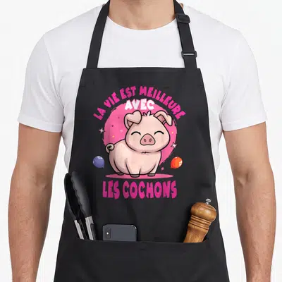 Tablier de cuisine noir avec illustration d'un cochon rose souriant entouré de ballons et d'étoiles sur fond circulaire rose.