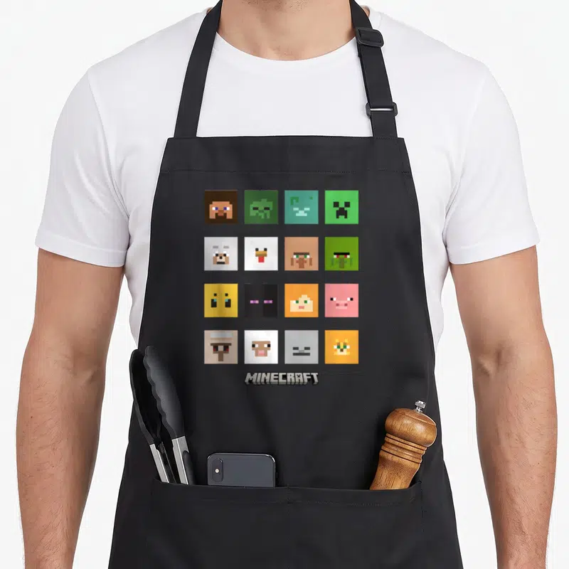 Tablier de cuisine noir avec une grille de visages pixelisés colorés représentant des créatures et ennemis du jeu Minecraft.