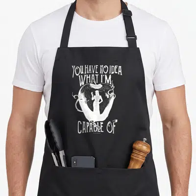 Tablier de cuisine noir avec une silhouette blanche dans une pomme et du texte stylisé.