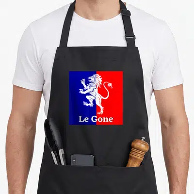 Tablier de cuisine noir avec un lion blanc rampant sur un fond divisé en bleu et rouge sous le texte Le Gone.