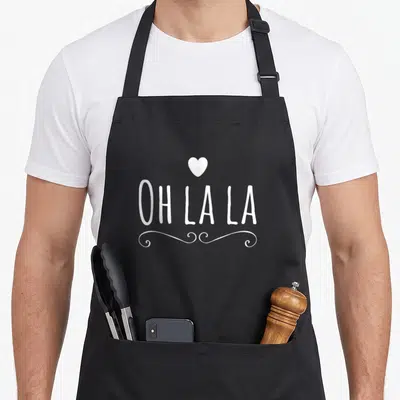 Tablier de cuisine noir avec inscription Oh la la, un cœur et des volutes décoratives en blanc au centre.
