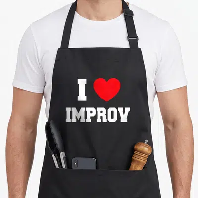 Tablier de cuisine noir avec un grand cœur rouge et le texte J adore l improv en lettres blanches majuscules.