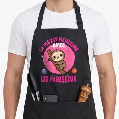 Tablier de cuisine noir avec un paresseux marron accroché à une branche sur un cercle rose et des étoiles.