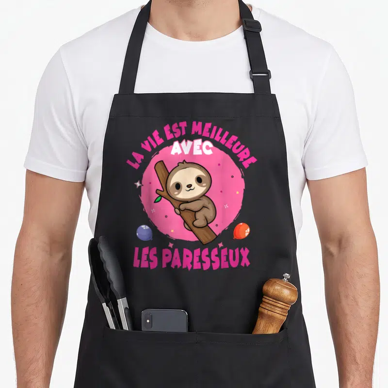 Tablier de cuisine noir avec un paresseux marron accroché à une branche sur un cercle rose et des étoiles.