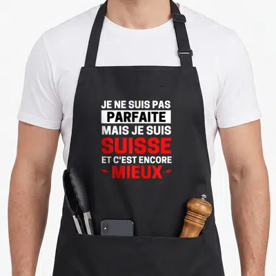 Tablier de cuisine noir avec l'inscription Je ne suis pas parfaite mais je suis Suisse encore mieux en lettres blanches et rouges.