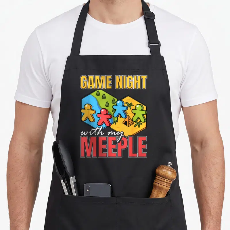 Tablier de cuisine noir avec illustration de pions de jeu de société multicolores sur des cases hexagonales et le texte Game Night with my Meeple.