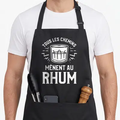 Tablier de cuisine noir avec illustration d'un verre de rhum et la phrase tous les chemins mènent au rhum en blanc.