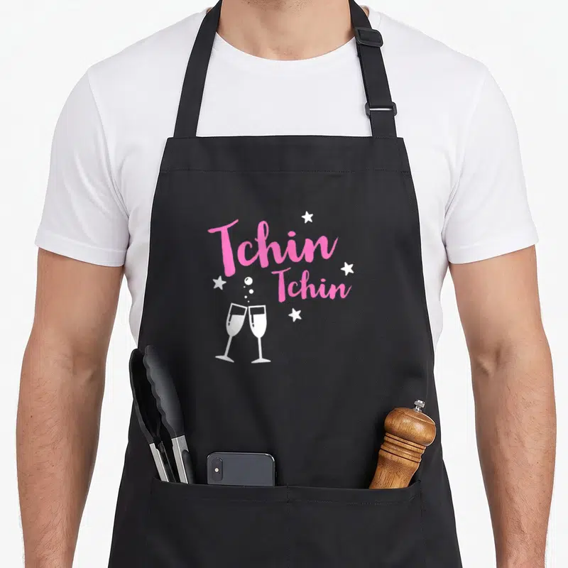 Tablier de cuisine noir avec deux verres de champagne et l'inscription Tchin Tchin en rose entouré d'étoiles blanches.