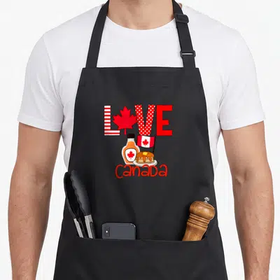 Tablier de cuisine noir avec illustration Love Canada, feuille d'érable, sirop et pancakes rouges et blancs.