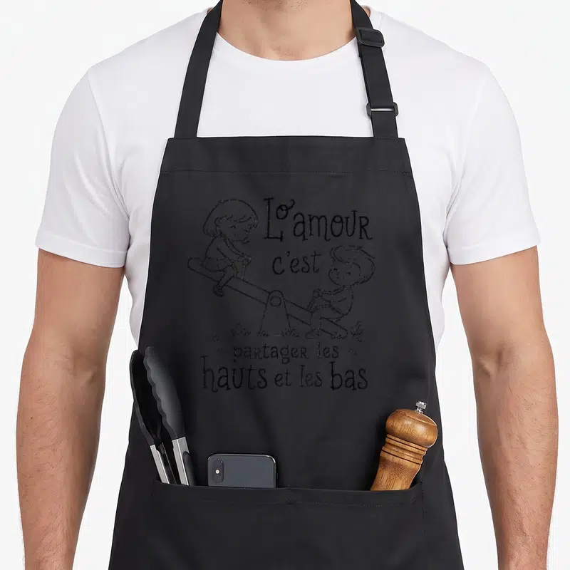 Tablier de cuisine noir avec illustration d'enfants sur une balançoire et texte L'amour c'est partager les hauts et les bas.