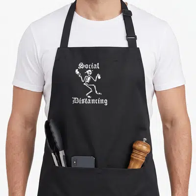 Tablier de cuisine noir avec un squelette blanc dansant tenant deux bouteilles et le texte Social Distancing en lettres gothiques.