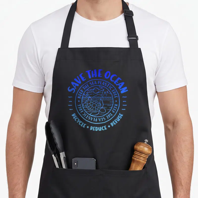 Tablier de cuisine noir avec logo circulaire bleu Save the Ocean illustrant une tortue et des consignes environnementales.