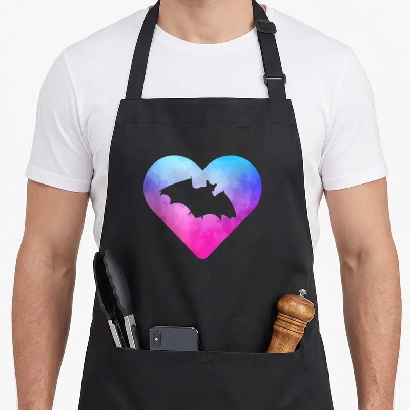 Tablier de cuisine noir avec un cœur aquarelle bleu et rose contenant la silhouette d'une chauve-souris noire.