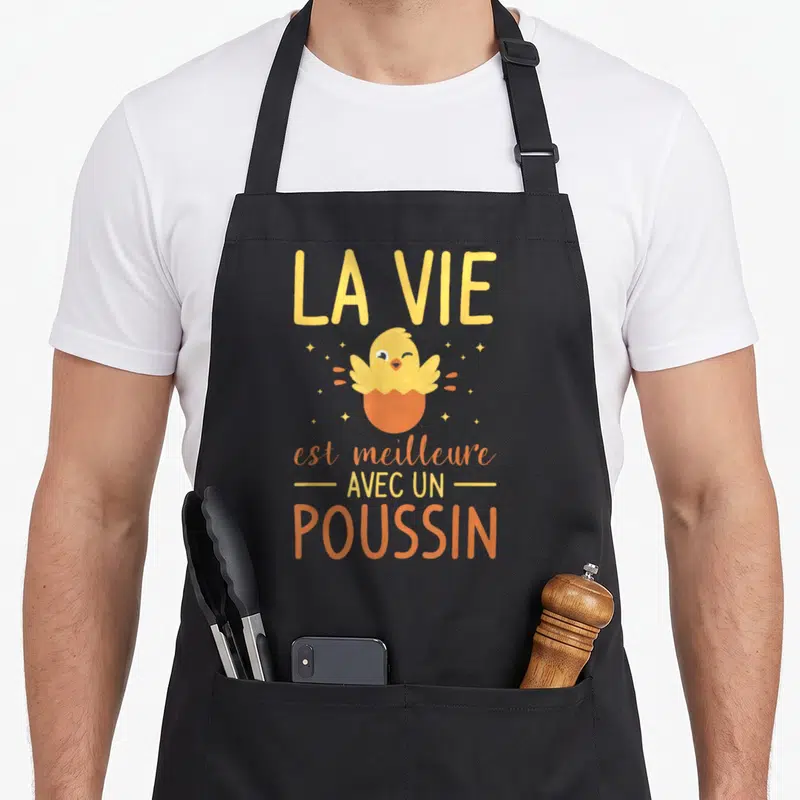 Tablier de cuisine noir avec illustration d'un poussin jaune sortant d'une coquille orange et des étoiles dorées.