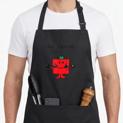 Tablier de cuisine noir avec Mr. Strong rouge levant des haltères et le nom Roger Hargreaves imprimé en haut.