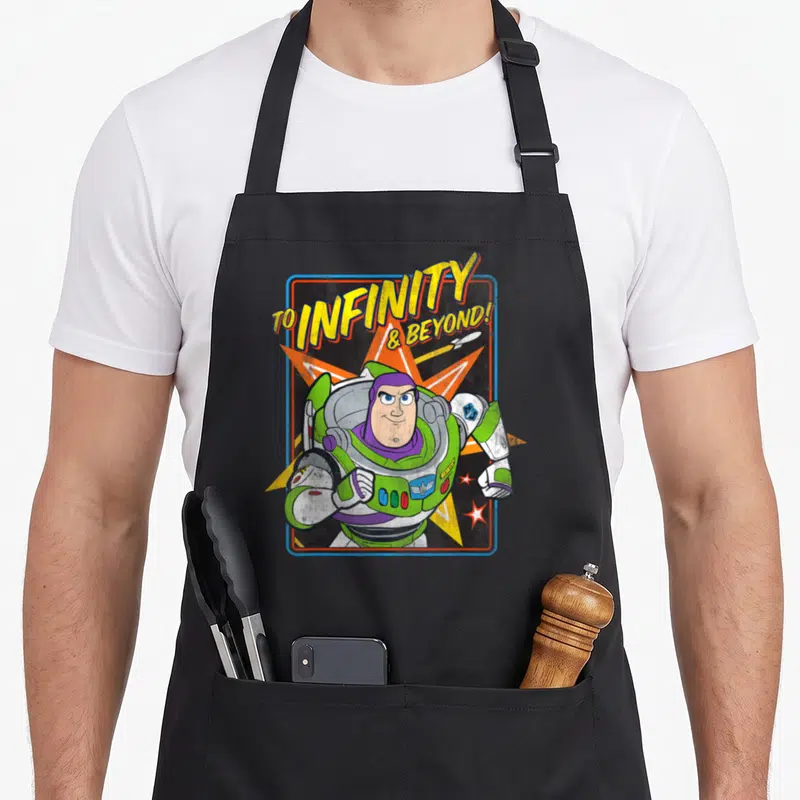 Tablier de cuisine noir avec illustration colorée de Buzz Lightyear et texte To Infinity & Beyond sur fond graphique rétro.