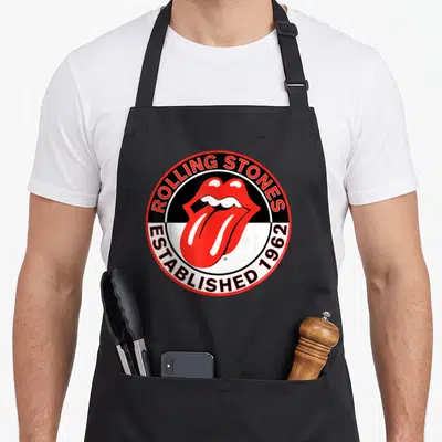 Tablier de cuisine noir avec l'emblème circulaire des Rolling Stones montrant une bouche rouge et les mots Established 1962.