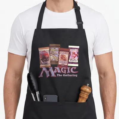 Tablier de cuisine noir avec le logo Magic The Gathering et quatre paquets de cartes à jouer vintage imprimés au centre.