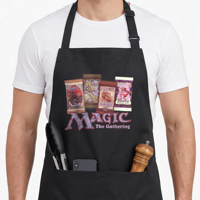 Tablier de cuisine noir avec le logo Magic The Rassemblement et quatre paquets de cartes à jouer vintage imprimés au centre.