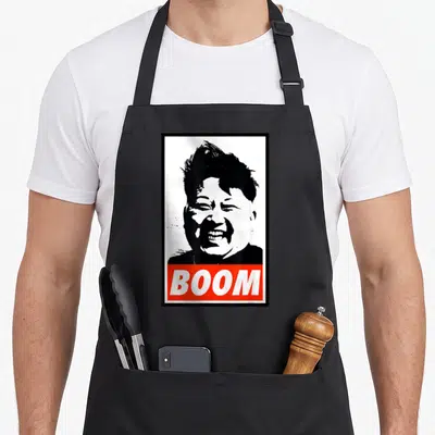 Tablier de cuisine noir avec portrait stylisé en noir et blanc et bande rouge portant le mot BOOM en blanc.
