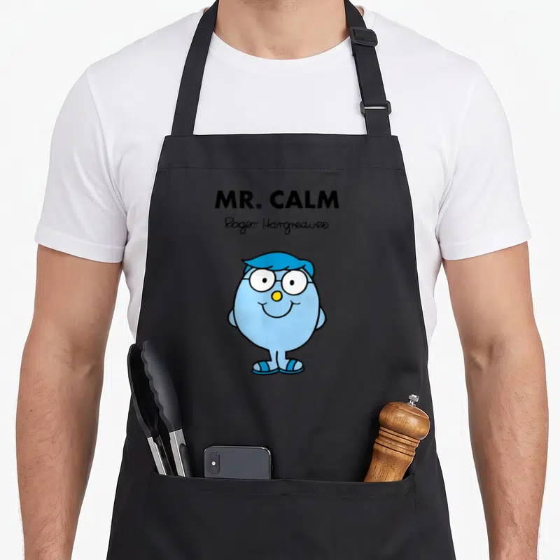 Tablier de cuisine noir avec illustration de Mr. Calm, personnage bleu souriant aux lunettes et signature Roger Hargreaves.