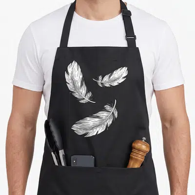 Tablier de cuisine noir avec trois plumes blanches dessinées au trait fin, disposées en triangle sur le devant.