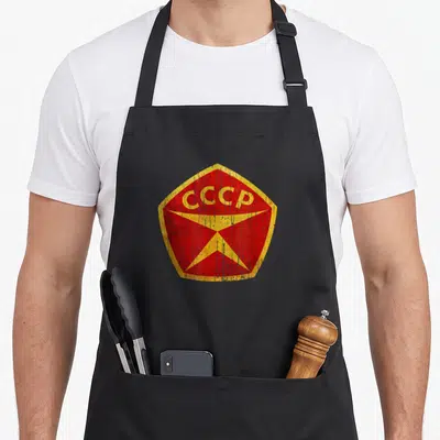 Tablier de cuisine noir avec un badge hexagonal rouge portant les lettres CCCP et une étoile jaune stylisée.
