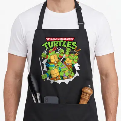 Tablier de cuisine noir avec les quatre tortues ninja bondissant et tenant leurs armes sous un logo vert et rouge.