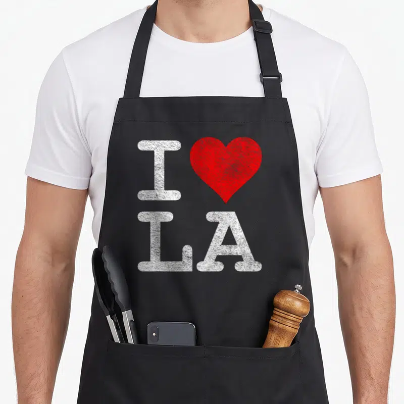 Tablier de cuisine noir avec un grand cœur rouge et les lettres I LA en blanc texturé.