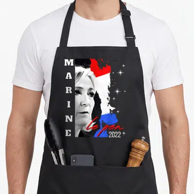 Tablier de cuisine noir avec portrait de Marine Le Pen, texte vertical et drapeau français stylisé en arrière-plan.