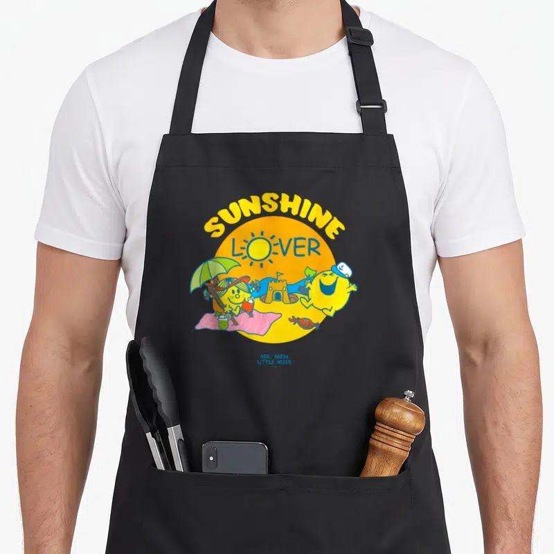 Tablier de cuisine noir avec illustration colorée d'un soleil jaune et de personnages Mr Men Little Miss sur une plage.