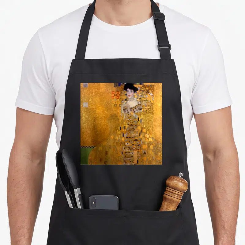 Tablier de cuisine noir avec le portrait de Gustav Klimt Bloch-Bauer aux motifs dorés et géométriques.
