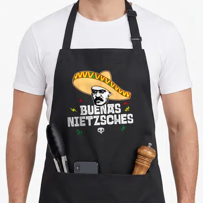 Tablier de cuisine noir avec illustration d'un sombrero, un visage de Nietzsche et le texte Buenas Nietzsches en blanc.