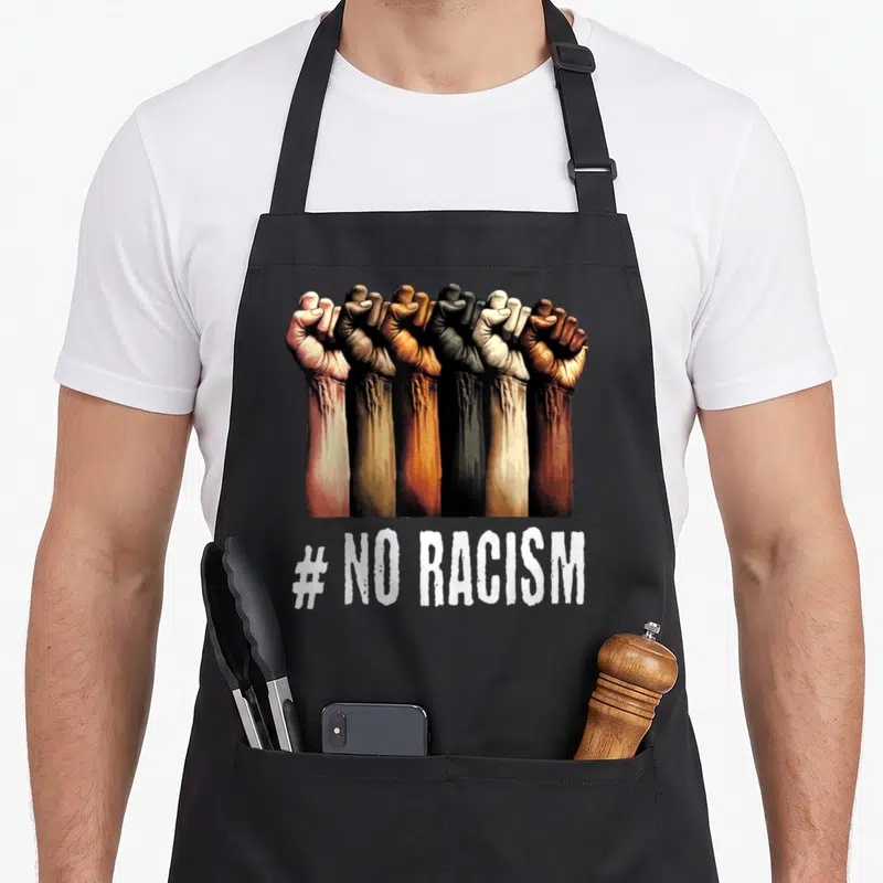 Tablier de cuisine noir avec cinq poings fermes de couleurs variées et l'inscription #NO RACISM en blanc.