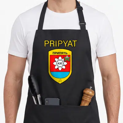 Tablier de cuisine noir avec les armoiries de Pripyat, un atome blanc et le texte PRIPYAT en jaune.