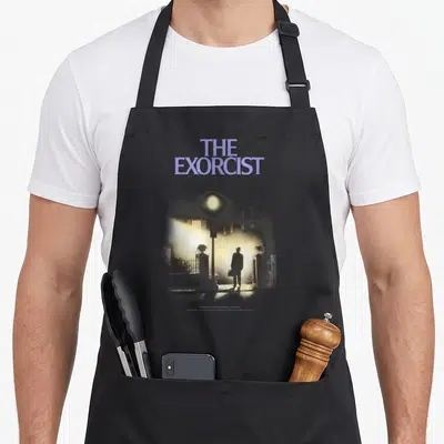 Tablier de cuisine noir avec une illustration de silhouette masculine sous un lampadaire et le titre The Exorcist en violet.