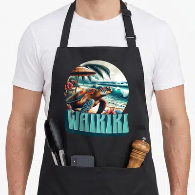 Tablier de cuisine noir avec illustration circulaire d'une tortue sur la plage et le texte Waikiki en bleu turquoise.