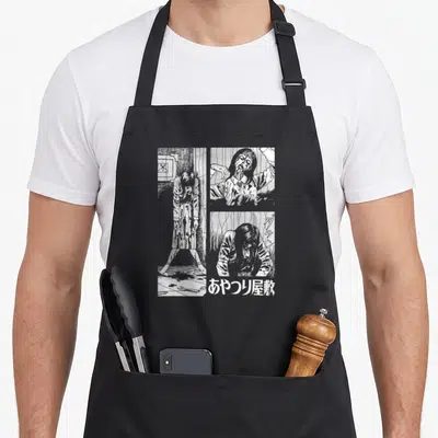 Tablier de cuisine noir avec une illustration en noir et blanc représentant des scènes d'horreur manga et du texte japonais en bas à droite.