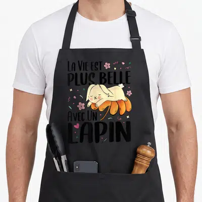 Tablier de cuisine noir avec un lapin beige dormant sur une fleur orange et des fleurs roses.