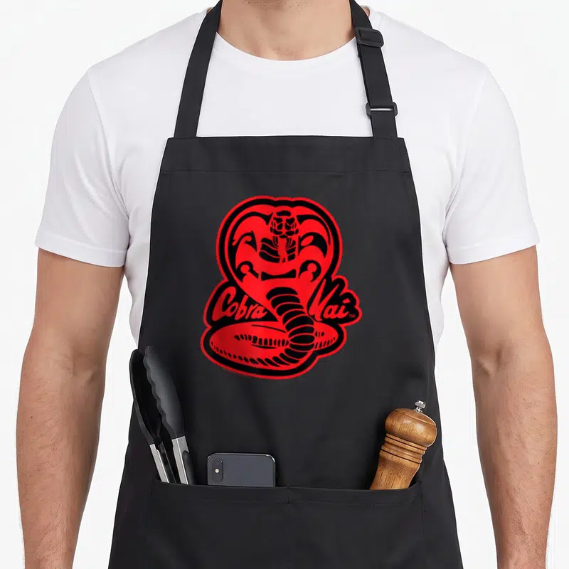 Tablier de cuisine noir avec un grand cobra rouge et noir et le texte Cobra Kai en lettres cursives.