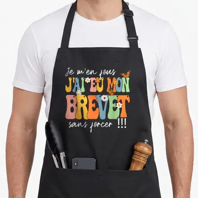 Tablier de cuisine noir avec typographie colorée Je m'en fous j'ai eu mon brevet sans forcer ornée de papillons et de fleurs.