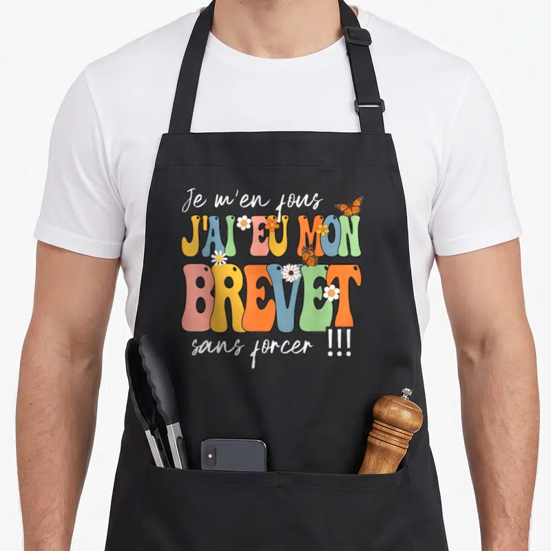 Tablier de cuisine noir avec typographie colorée Je m'en fous j'ai eu mon brevet sans forcer ornée de papillons et de fleurs.